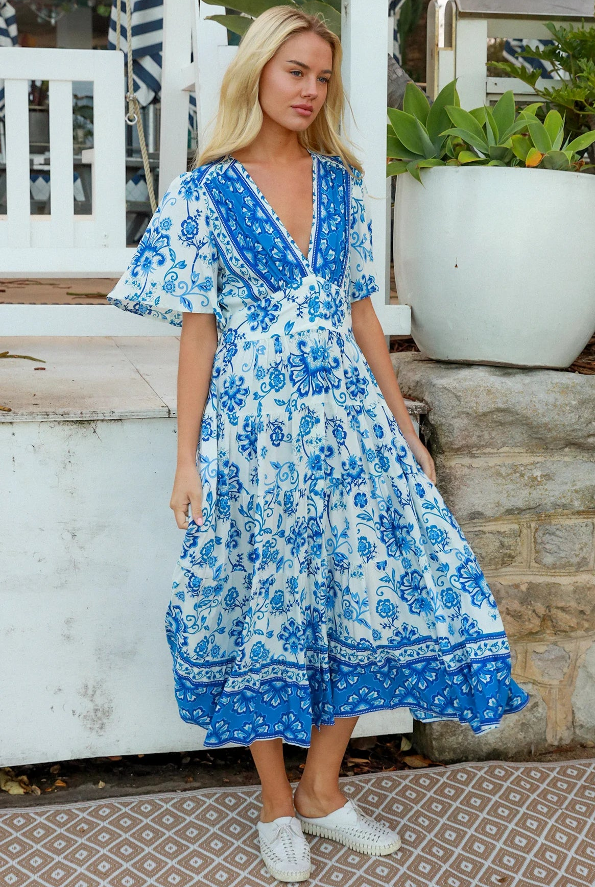 Woman in blue floral rayon bohemian midi dress with V-neckline flutter sleeves pockets and border frill hemline — Australia