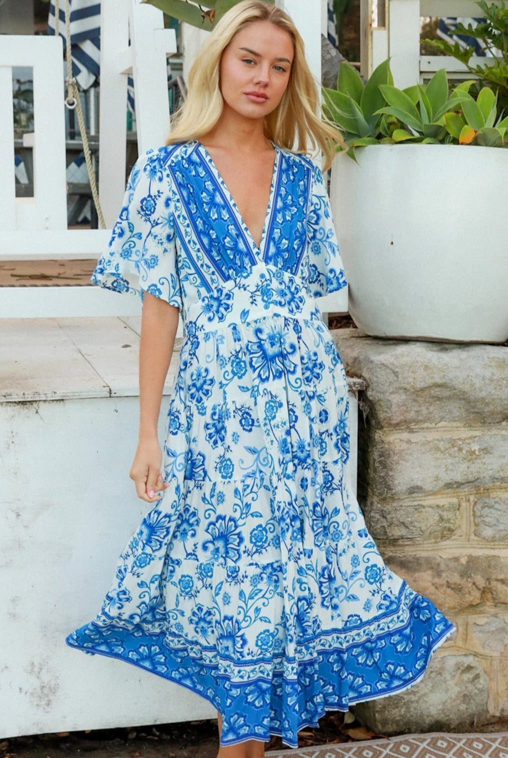 Woman in blue floral rayon bohemian midi dress with V-neckline flutter sleeves pockets and border frill hemline — Australia