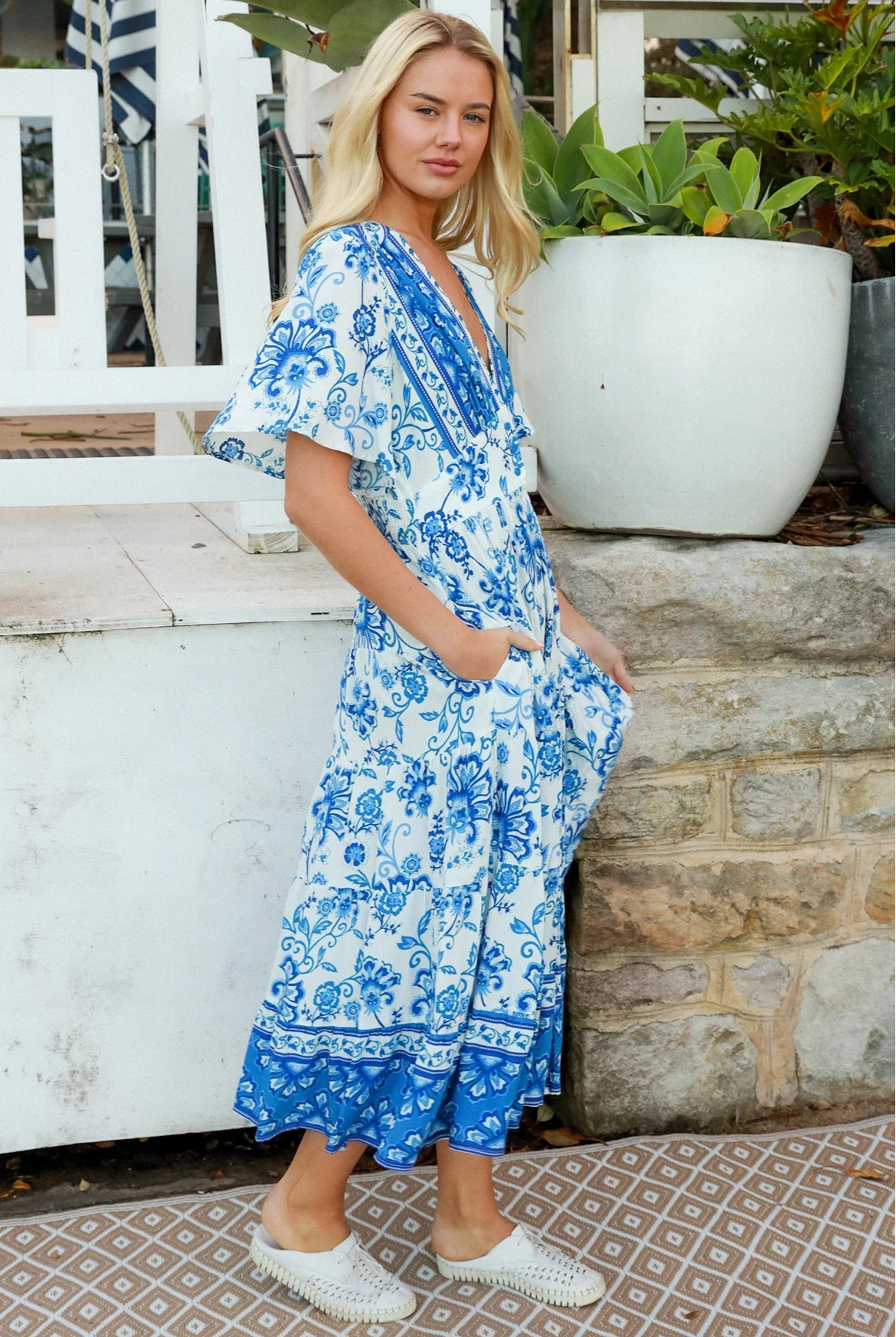 Woman in blue floral rayon bohemian midi dress with V-neckline flutter sleeves pockets and border frill hemline — Australia