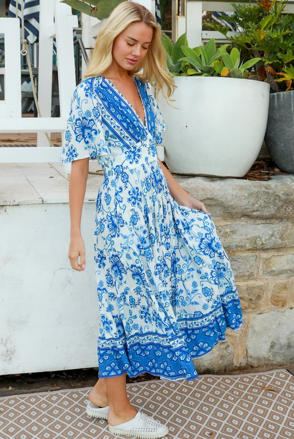 Woman in blue floral rayon bohemian midi dress with V-neckline flutter sleeves pockets and border frill hemline — Australia