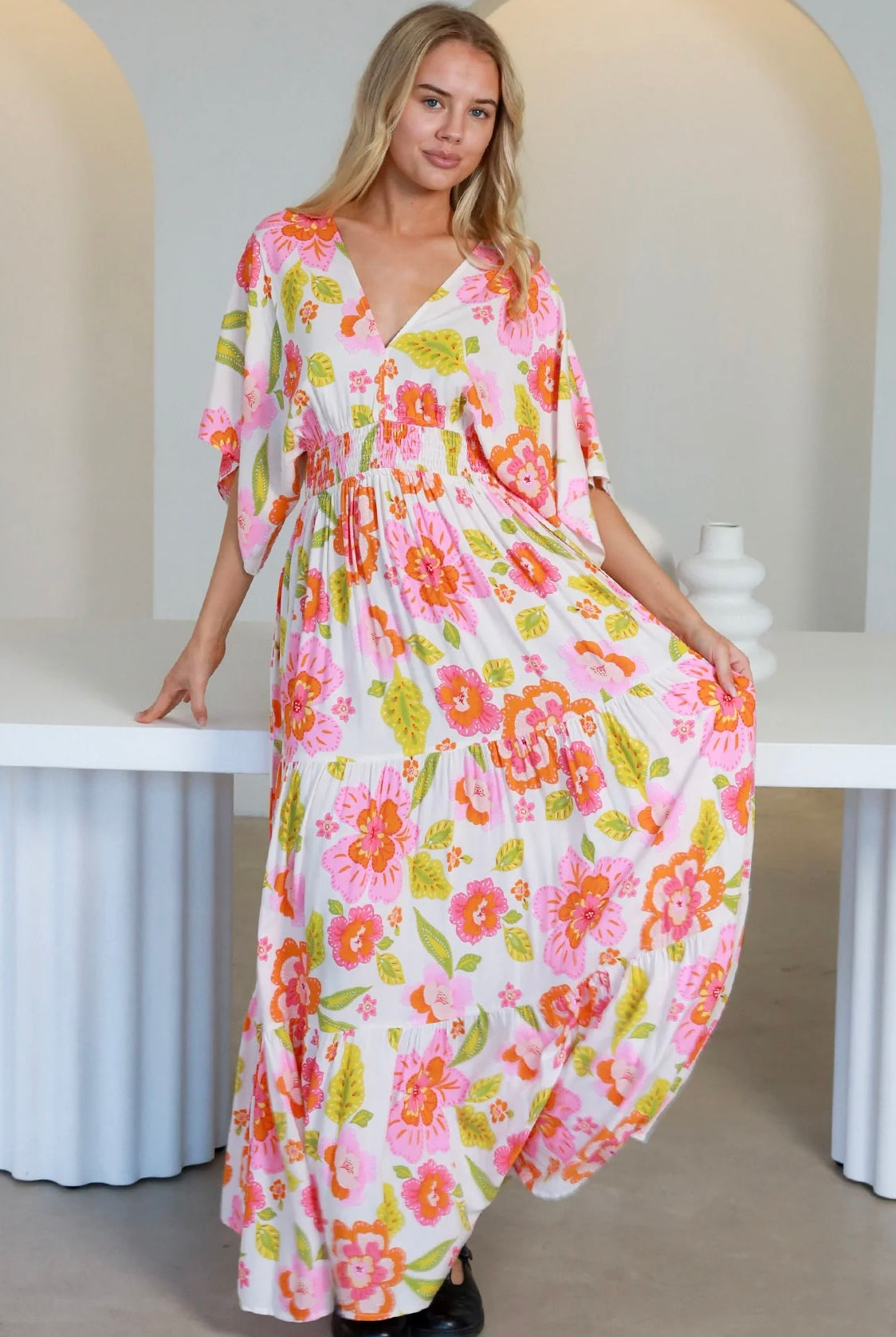 Woman in a coral-pink floral boho maxi dress with kimono sleeves - Isla Grace Tiered Maxi Dress Australia.