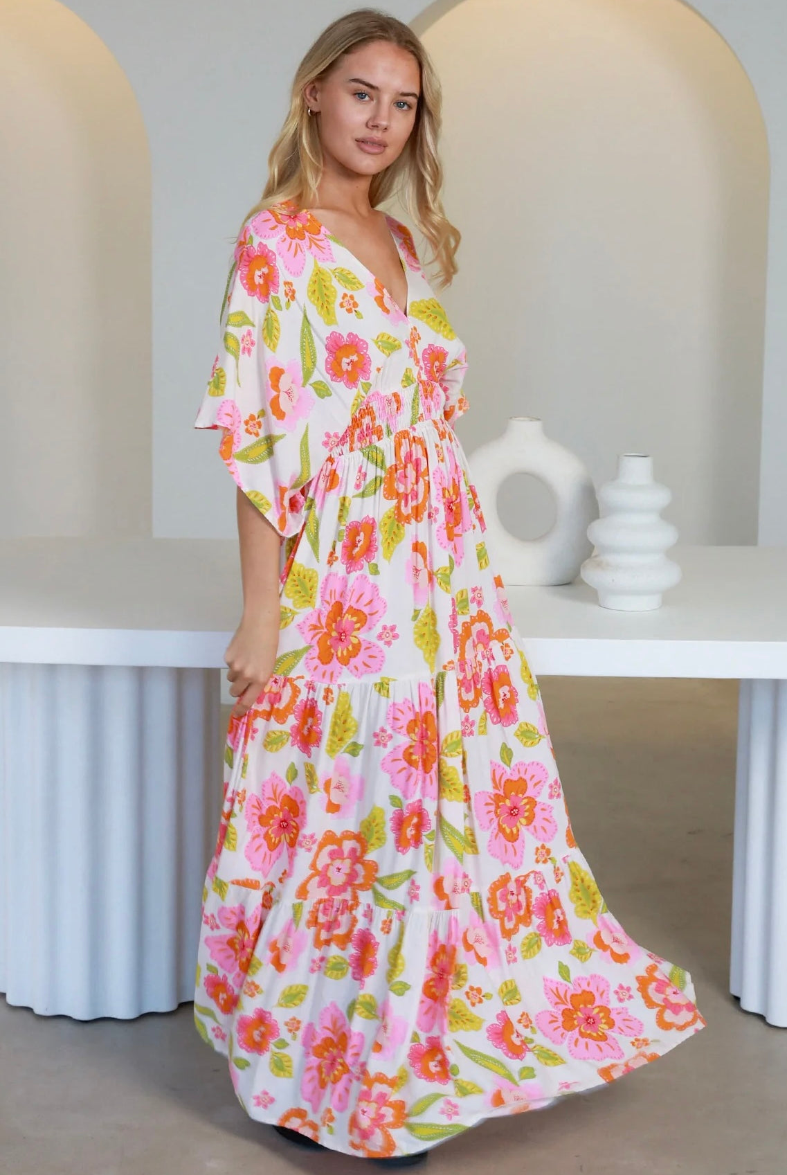 Woman in a coral-pink floral boho maxi dress with kimono sleeves - Isla Grace Tiered Maxi Dress Australia.