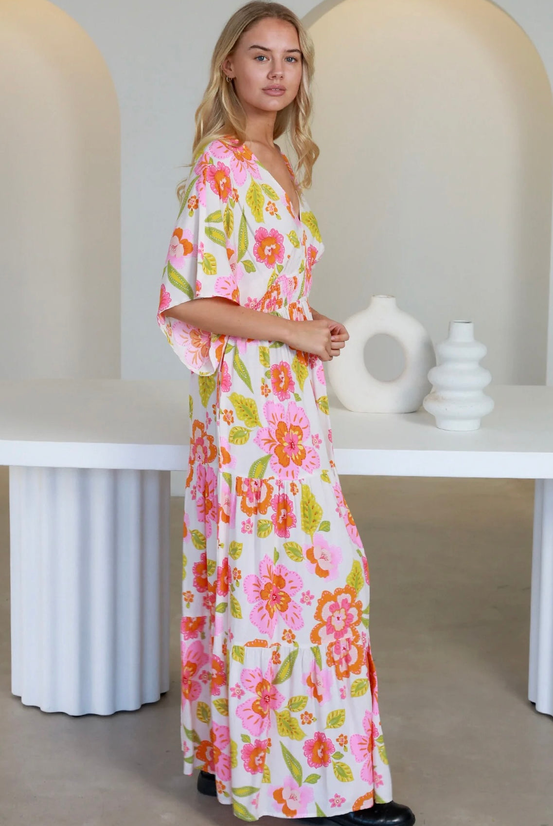 Woman in a coral-pink floral boho maxi dress with kimono sleeves - Isla Grace Tiered Maxi Dress Australia.