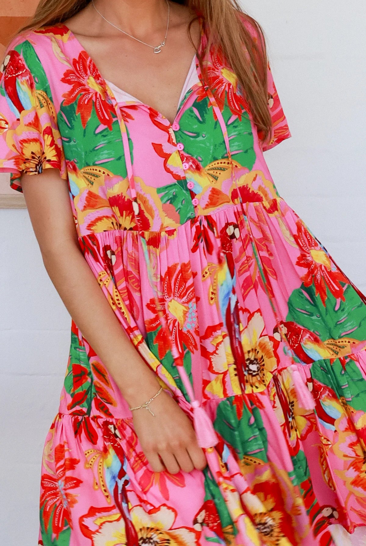 Pink floral mini dress with poppy and parrot print, V-neck button bodice, tassel ties and flutter sleeves