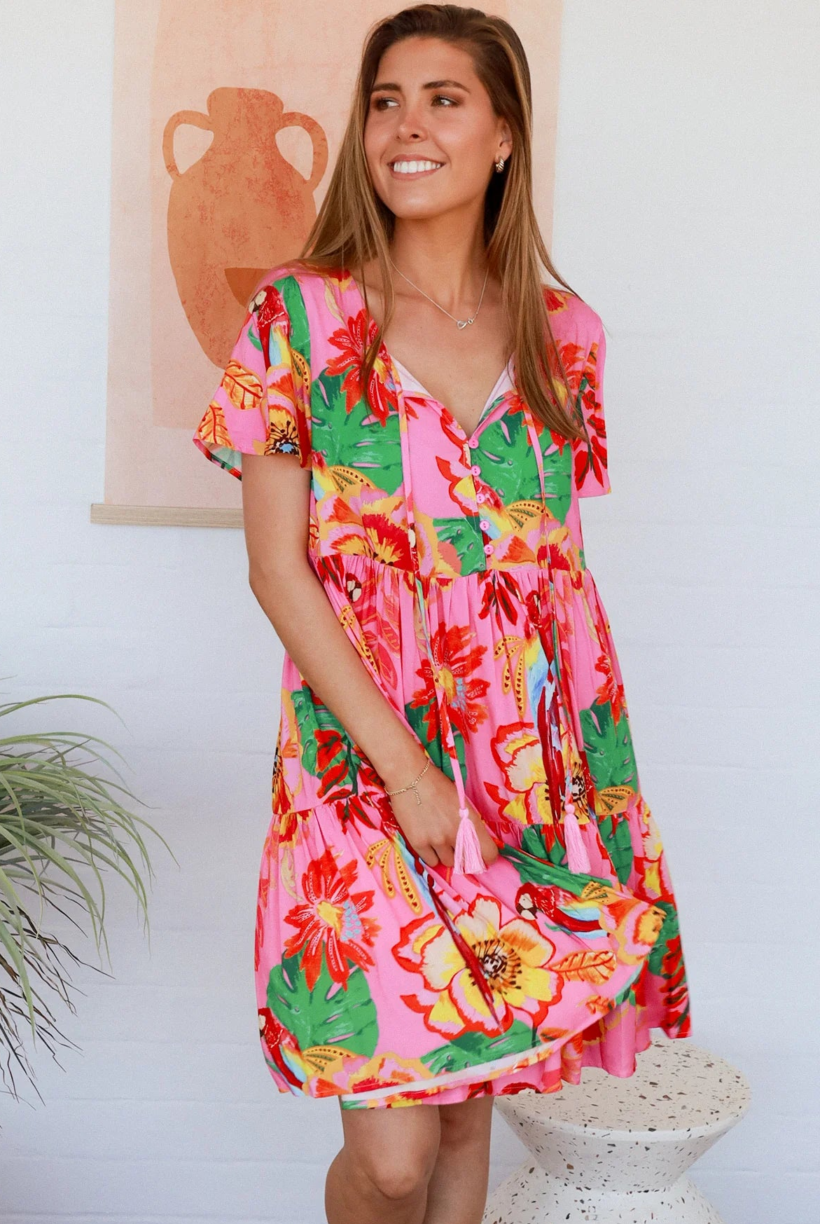 Pink floral mini dress with poppy and parrot print, V-neck button bodice, tassel ties and flutter sleeves