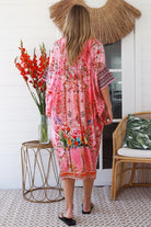 “Woman in pink floral viscose crepe kaftan midi dress with rhinestone buttons by Peacock Feathers – bohemian resort wear Australia”