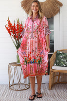 “Woman in pink floral viscose crepe kaftan midi dress with rhinestone buttons by Peacock Feathers – bohemian resort wear Australia”