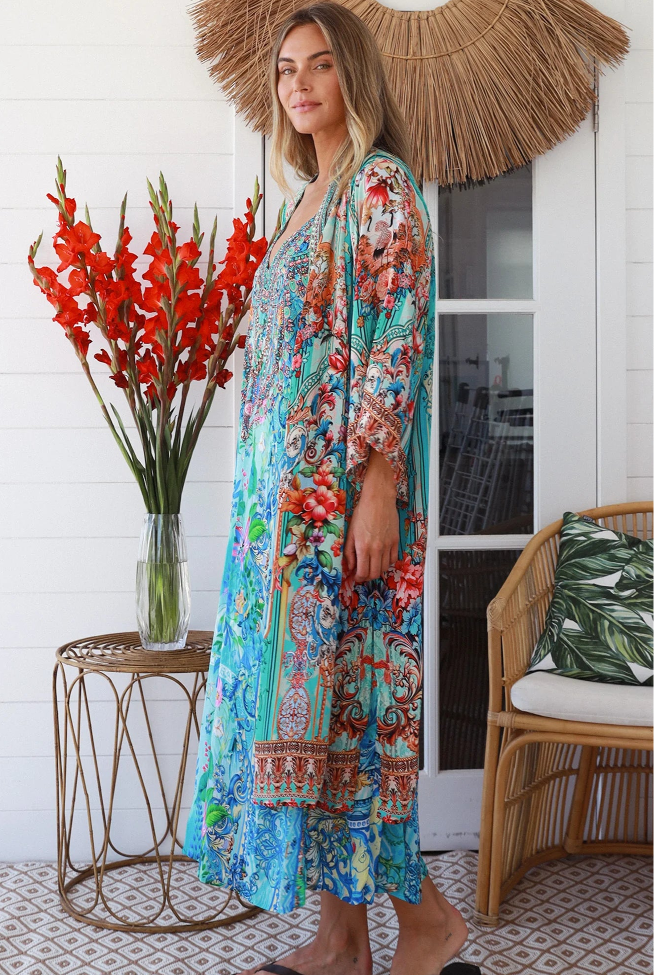Woman in turquoise floral crepe - viscose kimono with bronze and sapphire border detailing, walking along a sunlit coastal setting - resort luxe boho style.