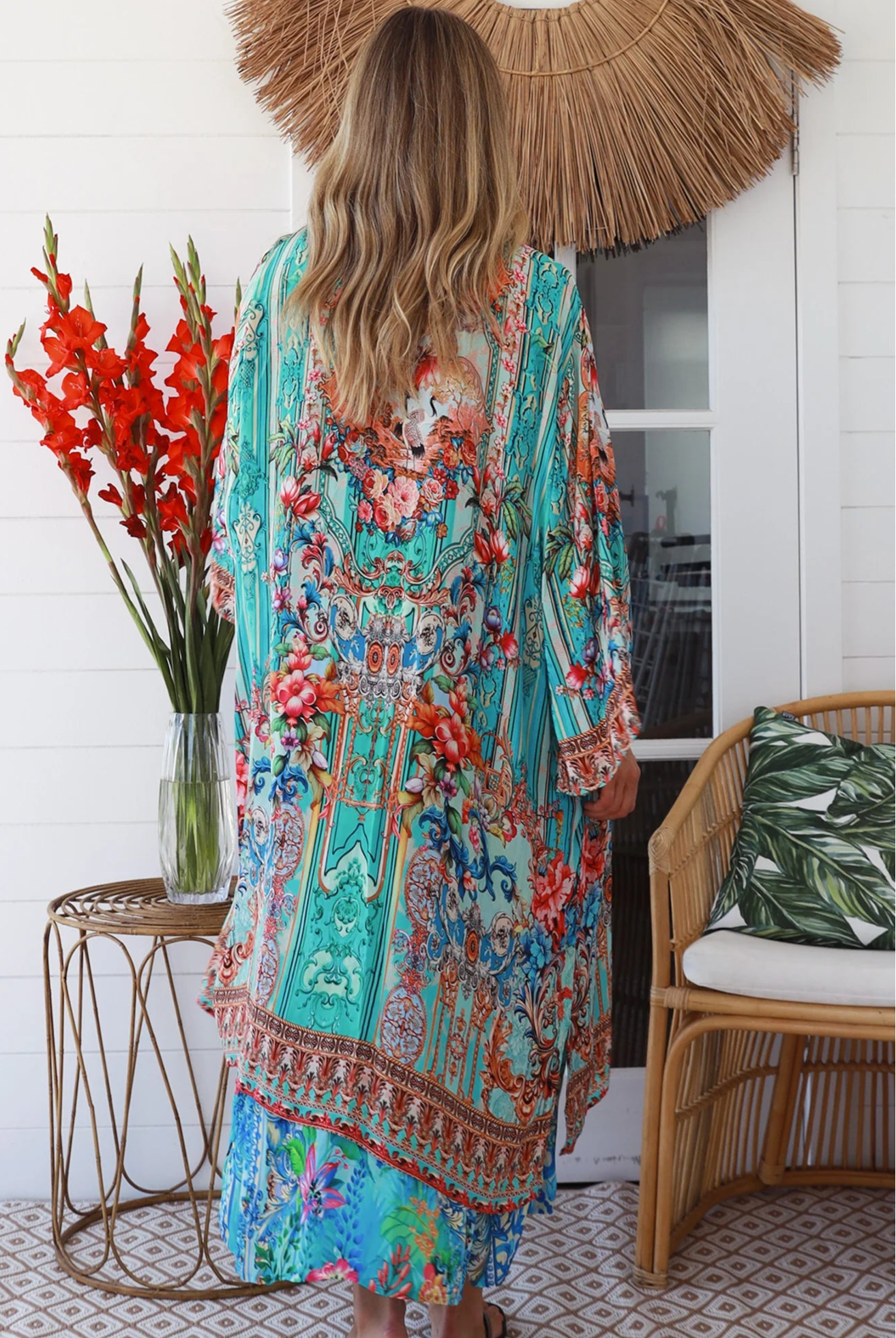 Woman in turquoise floral crepe - viscose kimono with bronze and sapphire border detailing, walking along a sunlit coastal setting - resort luxe boho style.
