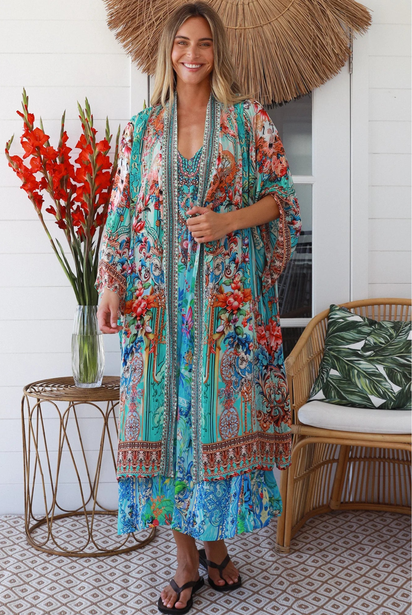 Woman in turquoise floral crepe - viscose kimono with bronze and sapphire border detailing, walking along a sunlit coastal setting - resort luxe boho style.
