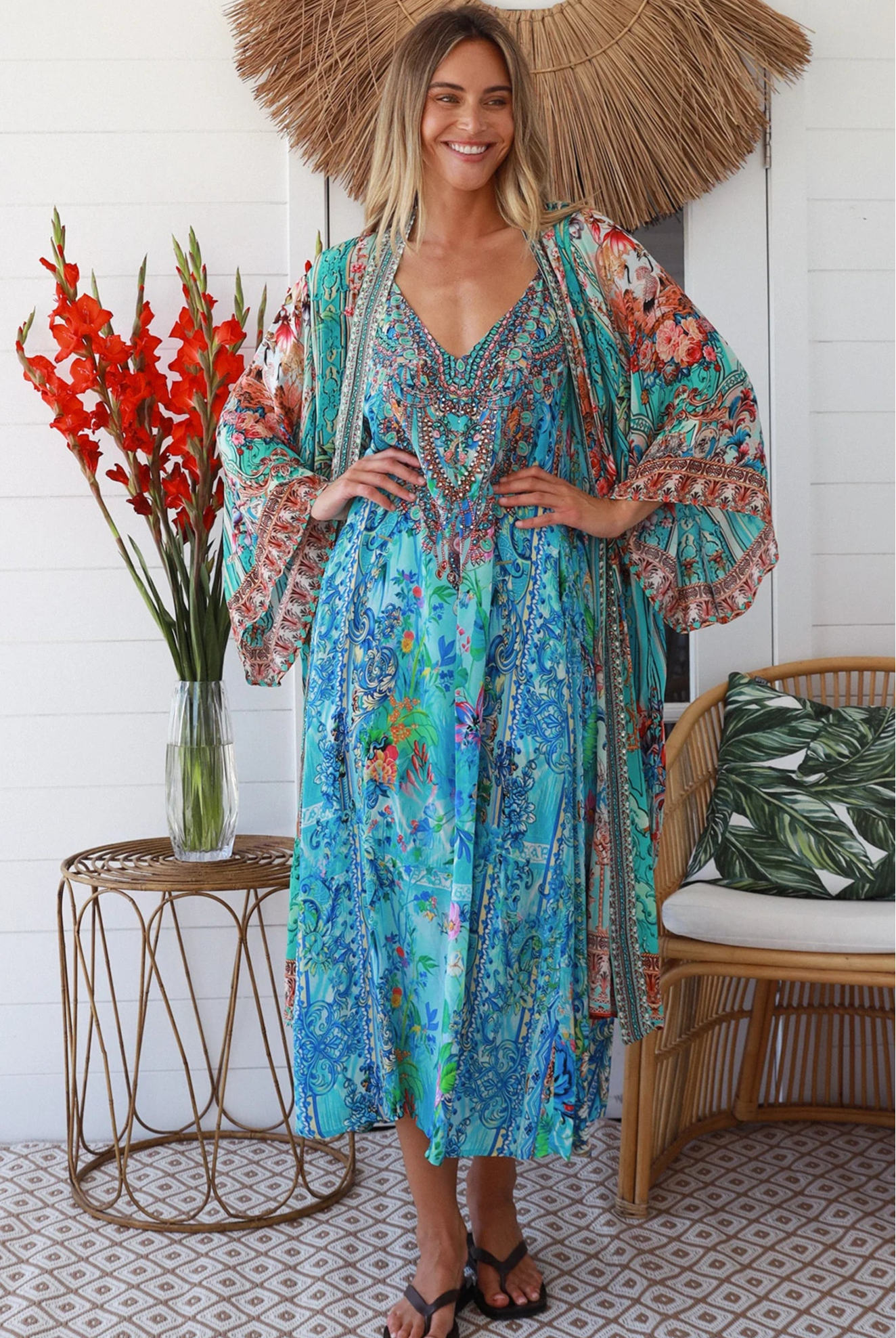 Woman in turquoise floral crepe - viscose kimono with bronze and sapphire border detailing, walking along a sunlit coastal setting - resort luxe boho style.