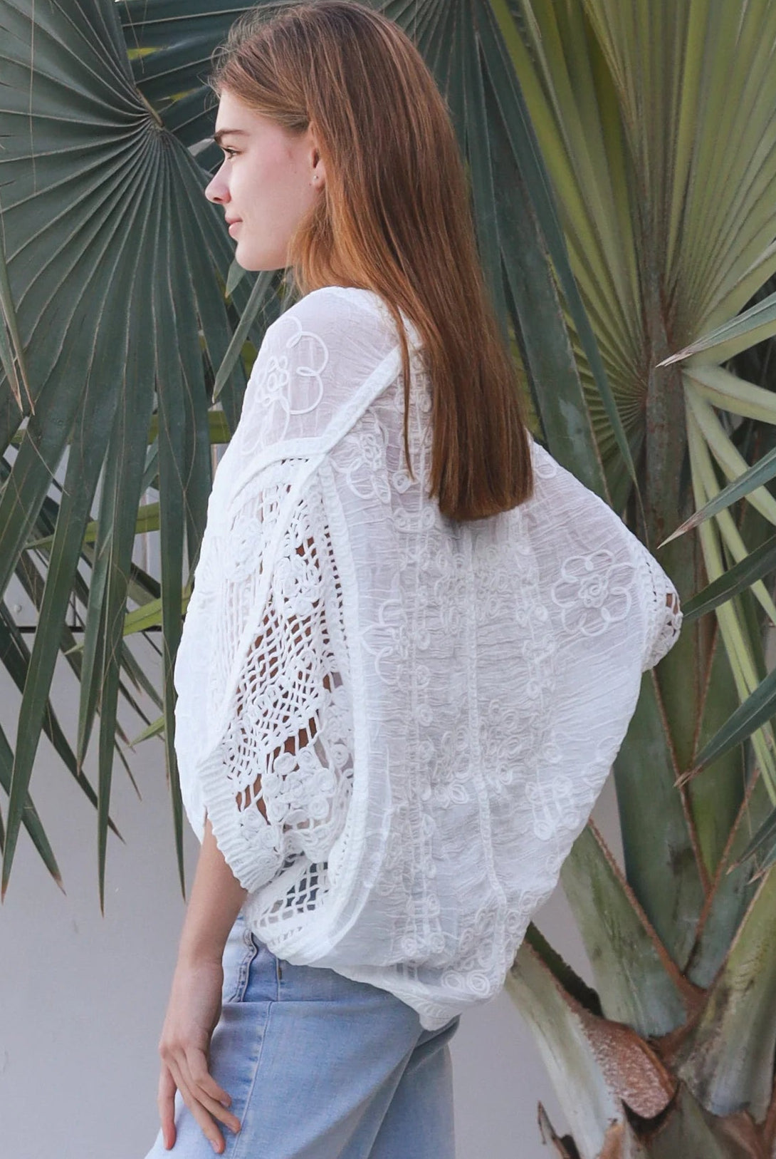 Woman wearing oversized white embroidered cotton crochet blouse with airy sleeves and relaxed coastal bohemian styling in Australia