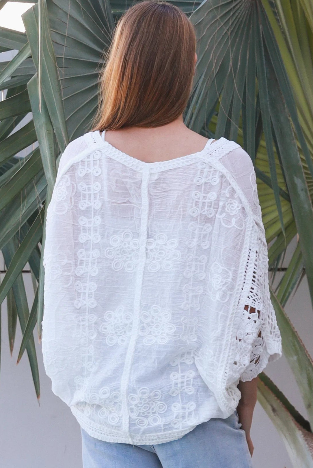 Woman wearing oversized white embroidered cotton crochet blouse with airy sleeves and relaxed coastal bohemian styling in Australia