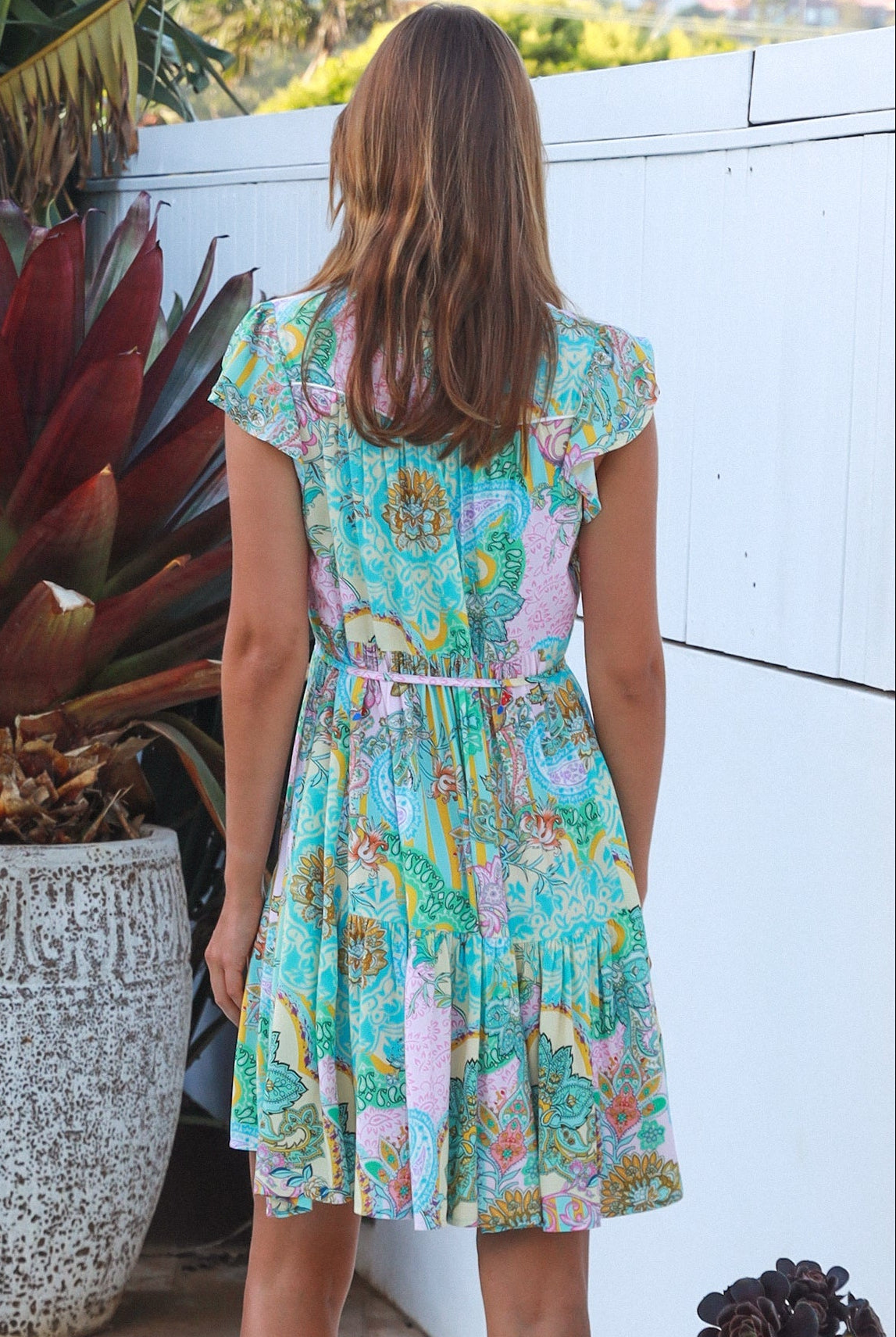 Woman wearing a green and pink painterly patchwork rayon mini dress with flutter sleeves and waist tie by Salty Palm