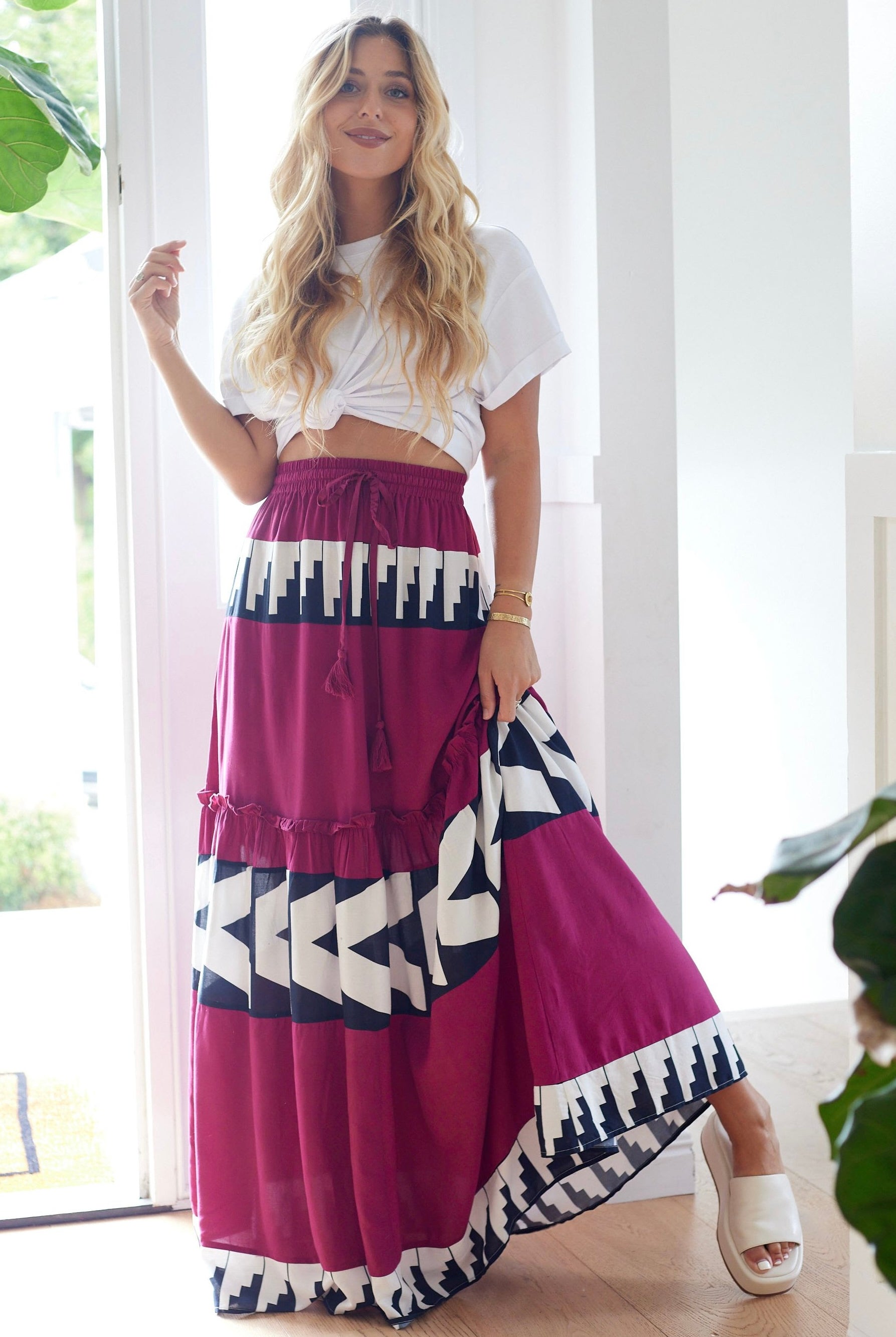Woman wearing a white top and a long, patterned skirt with geometric designs indoors.