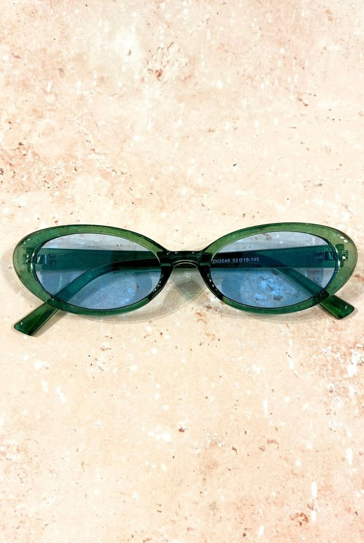 Green retro oval sunglasses with blue tinted lenses styled on stone background - vintage flat lay eyewear Australia.