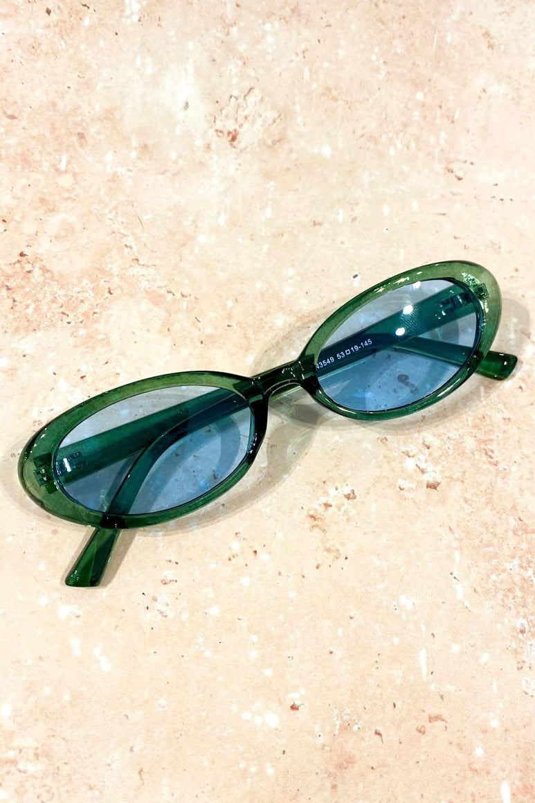 Green retro oval sunglasses with blue tinted lenses styled on stone background - vintage flat lay eyewear Australia.