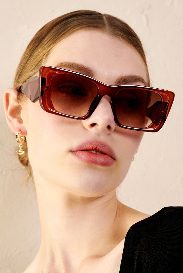 Woman in brown oversized cat eye sunglasses with sleek bun and black top - vintage boho style Australia.
