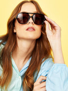 Women in Quinn Aviator sunglasses with tousled waves and blue shirt - vintage boho style against yellow backdrop Australia.