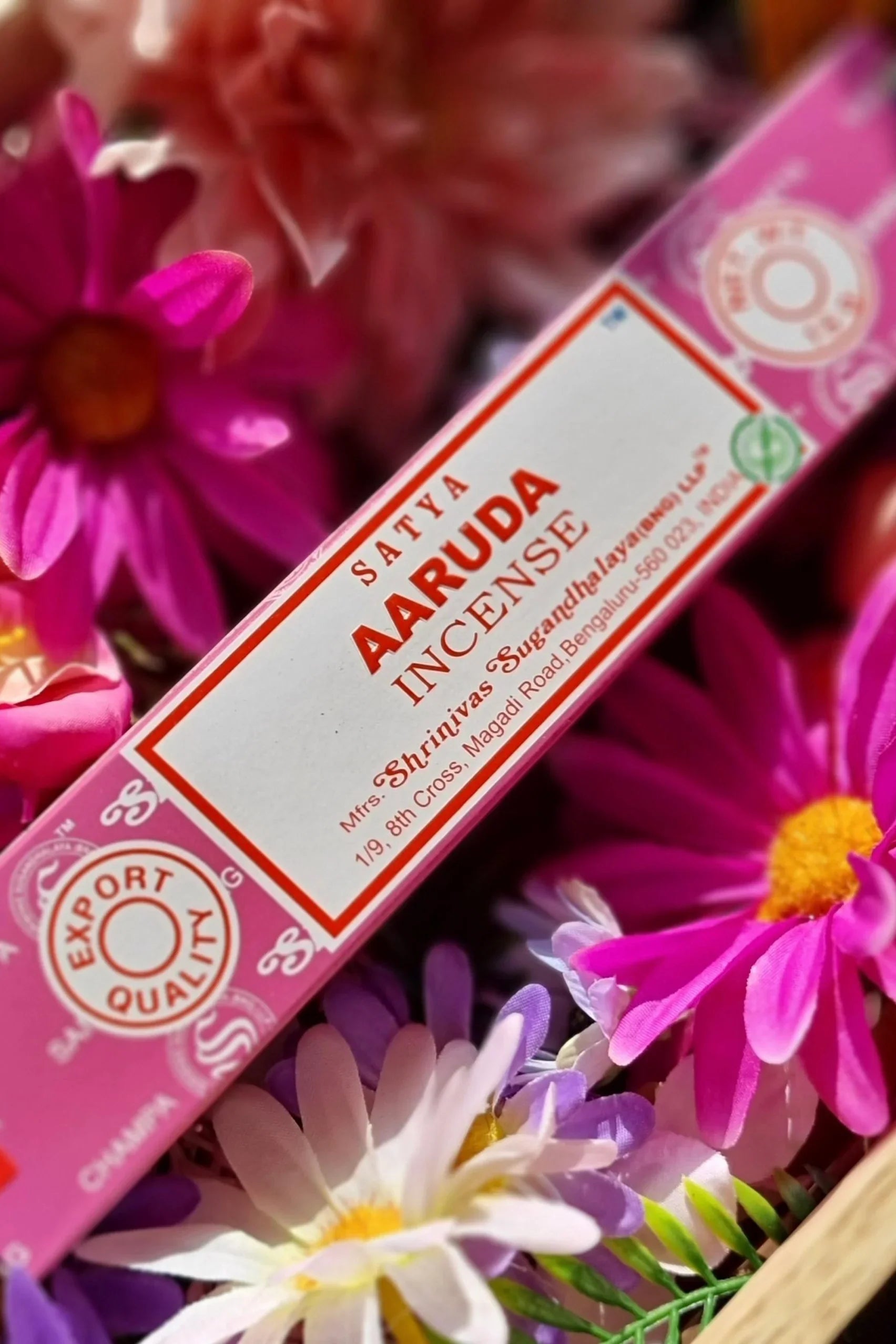 Sataya Aaruda incense sticks in pink packaging surrounded by vibrand fresh flowers, styled in a bohemian - inspired flat lay.
