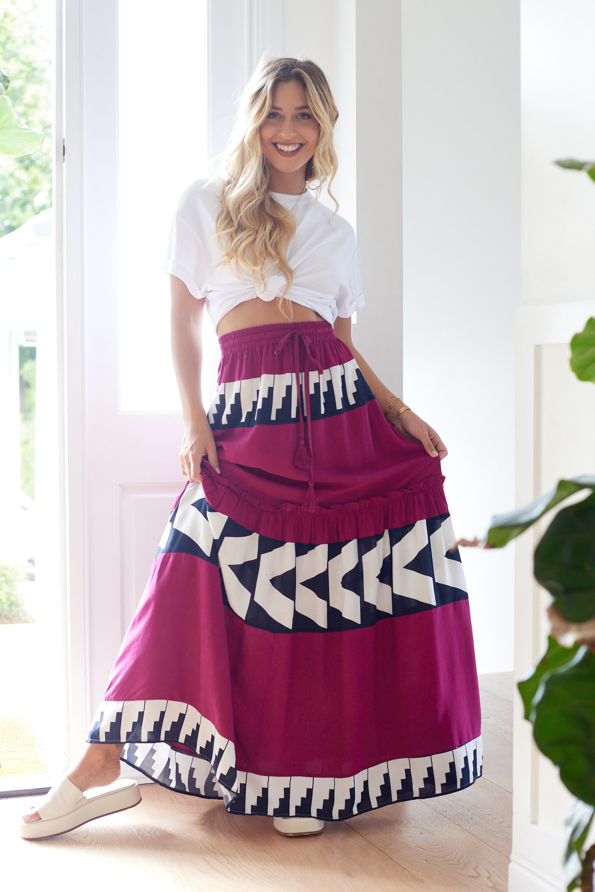 Model wearing romantic boho maxi skirt in  deep magenta with bold white and black feometric panels, styled with a knotted white top in a sunlit space.