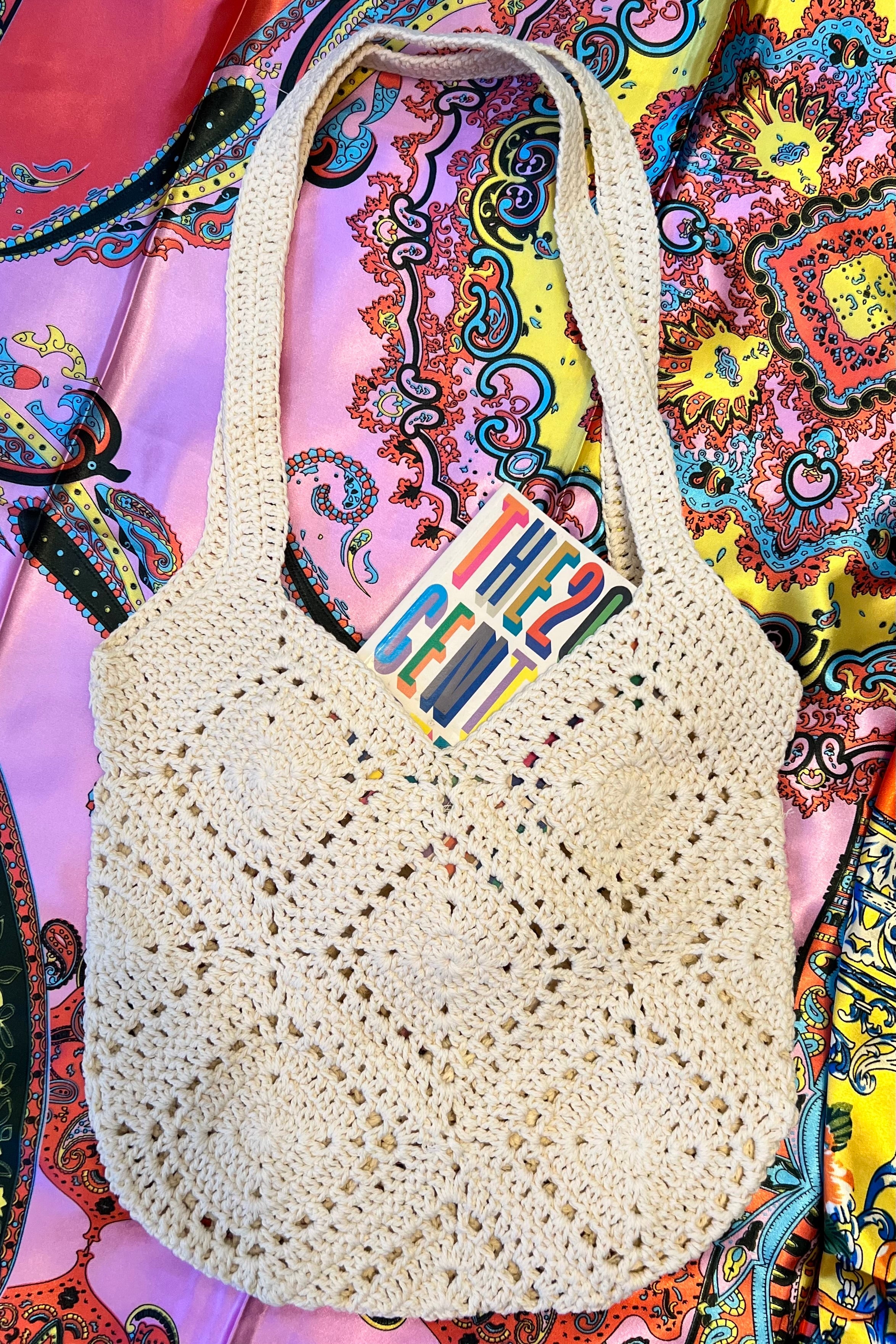 Natural crochet shoulder bag with diamond pattern, styled on vibrant boho fabric backdrop.