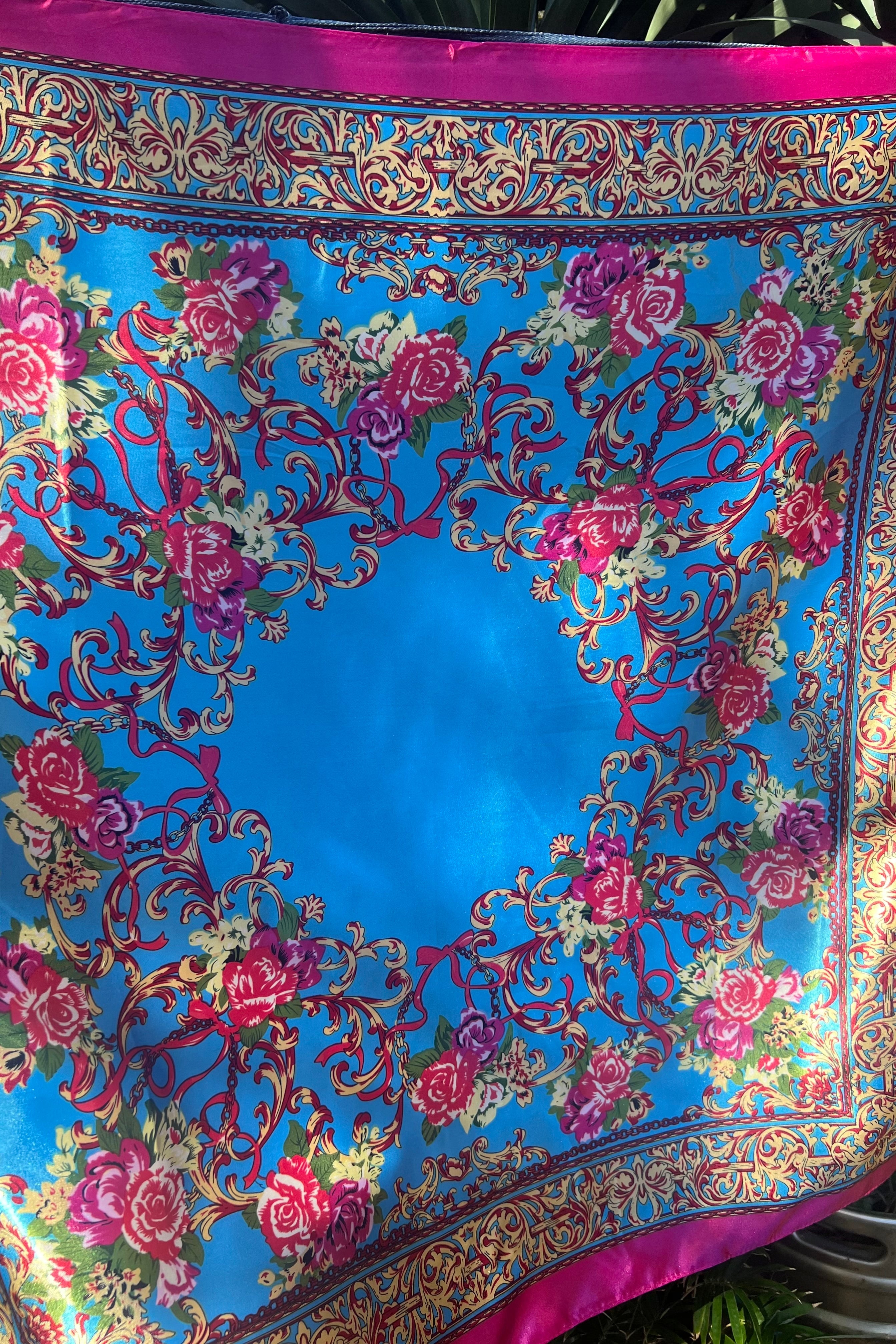 Baroque-style square scarf in bright blue with ornate gold scrollwork, pink rose detailing, and a magenta border, displayed outdoor with natural light.