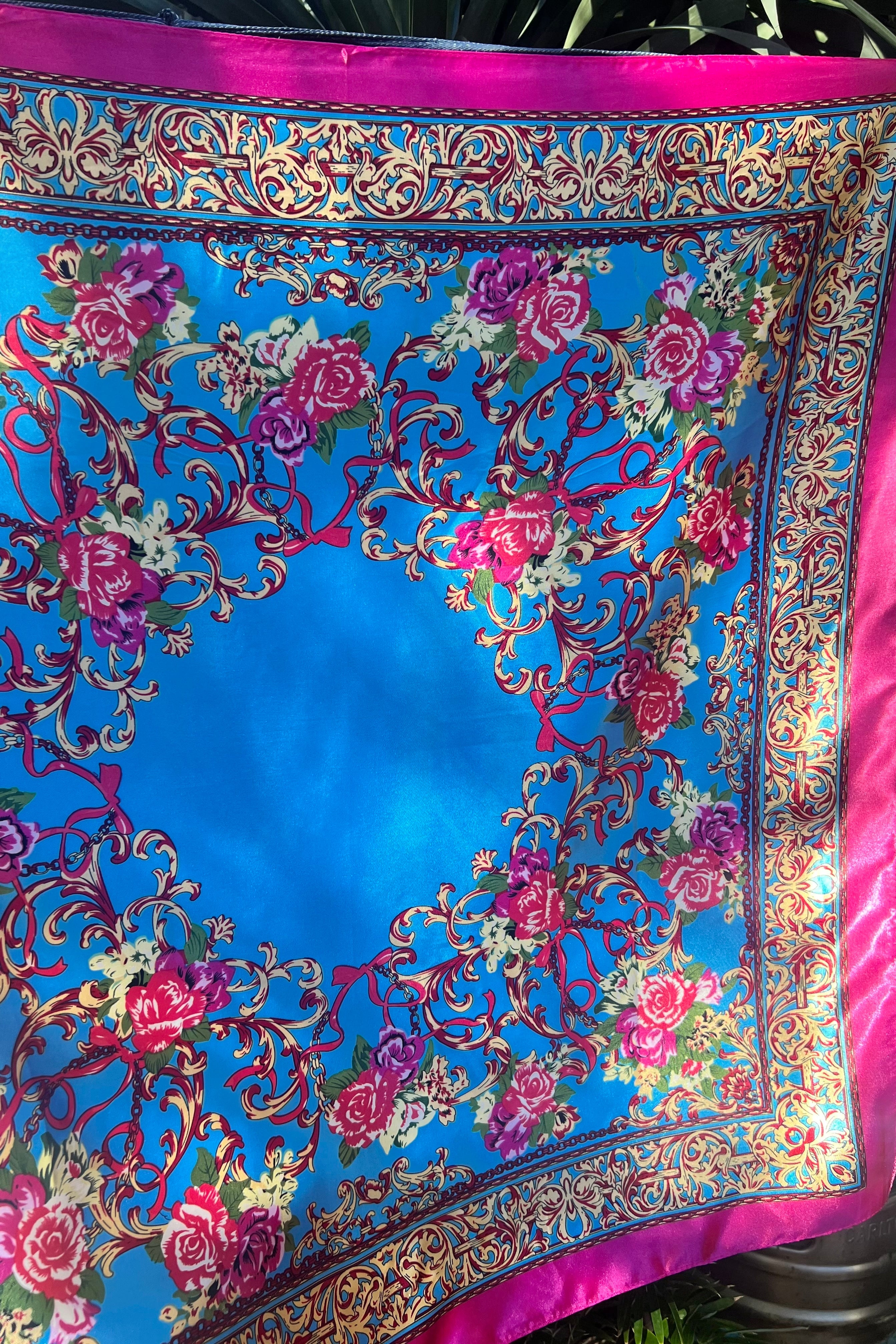 Square satin scarf with a vivid cobalt blue middle, bordered by intricate pink floral and gold baroque detailing, shown laid flat with hot pink edging.
