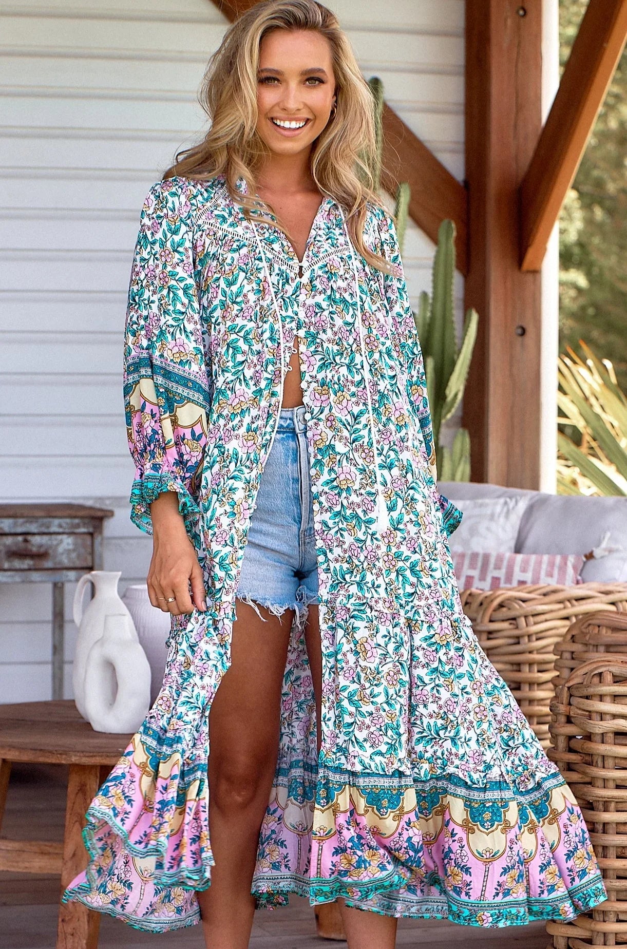 smiling woman in long floral JAASE duster with pink and green boho print over denim shorts - barefoot Australia boho style.