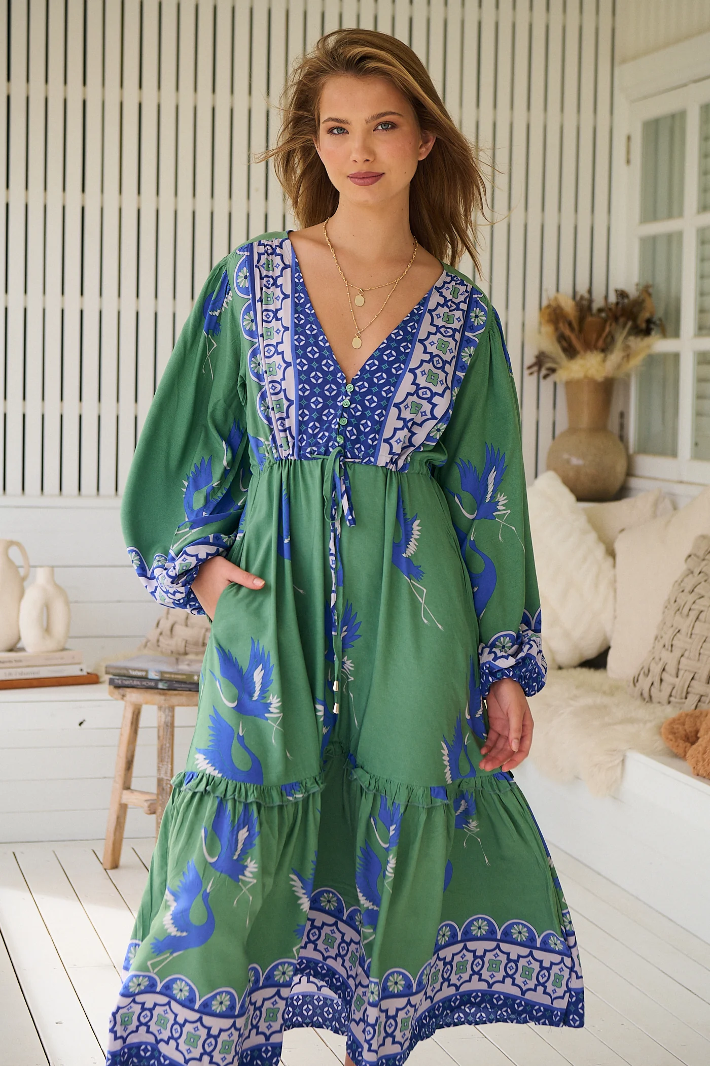 Model wearing a jade green bohemian maxi dress with a blue floral border print, long billowed sleeves, deep v-neckline, and drawstring waist - romantic boho style.
