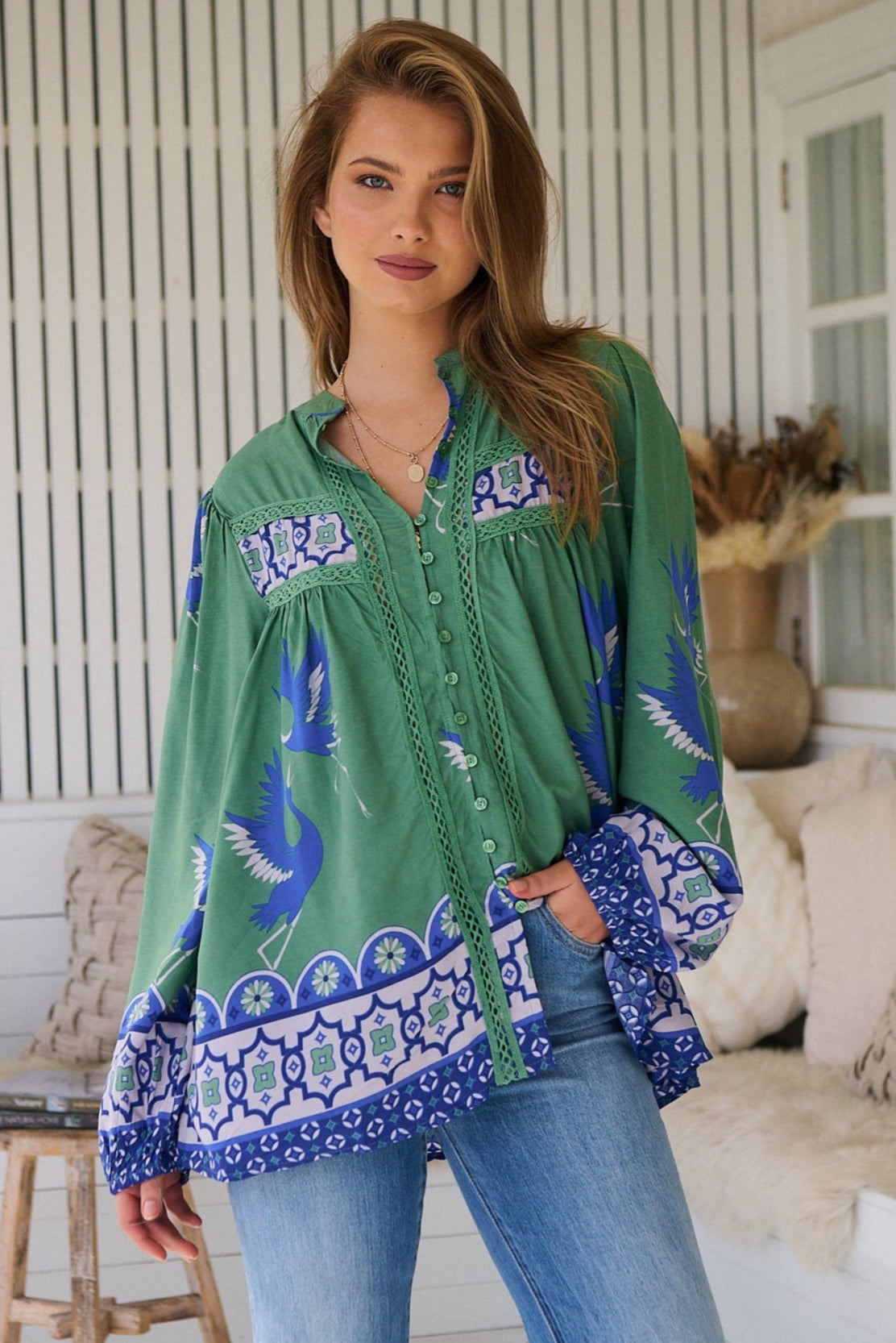 Model wearing green boho blouse with with blue border print and billowed sleeves - relaxed silhouette styled with jeans for modern bohemian fashion.