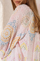 A close-up of a woman wearing a light pink eyelet embroidered top with pastel multicolor mandala and floral patterns.