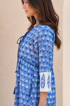 A woman wearing a blue and white floral block-printed dress, shown from a side profile against a neutral beige wall from Bohemian Love Runway.