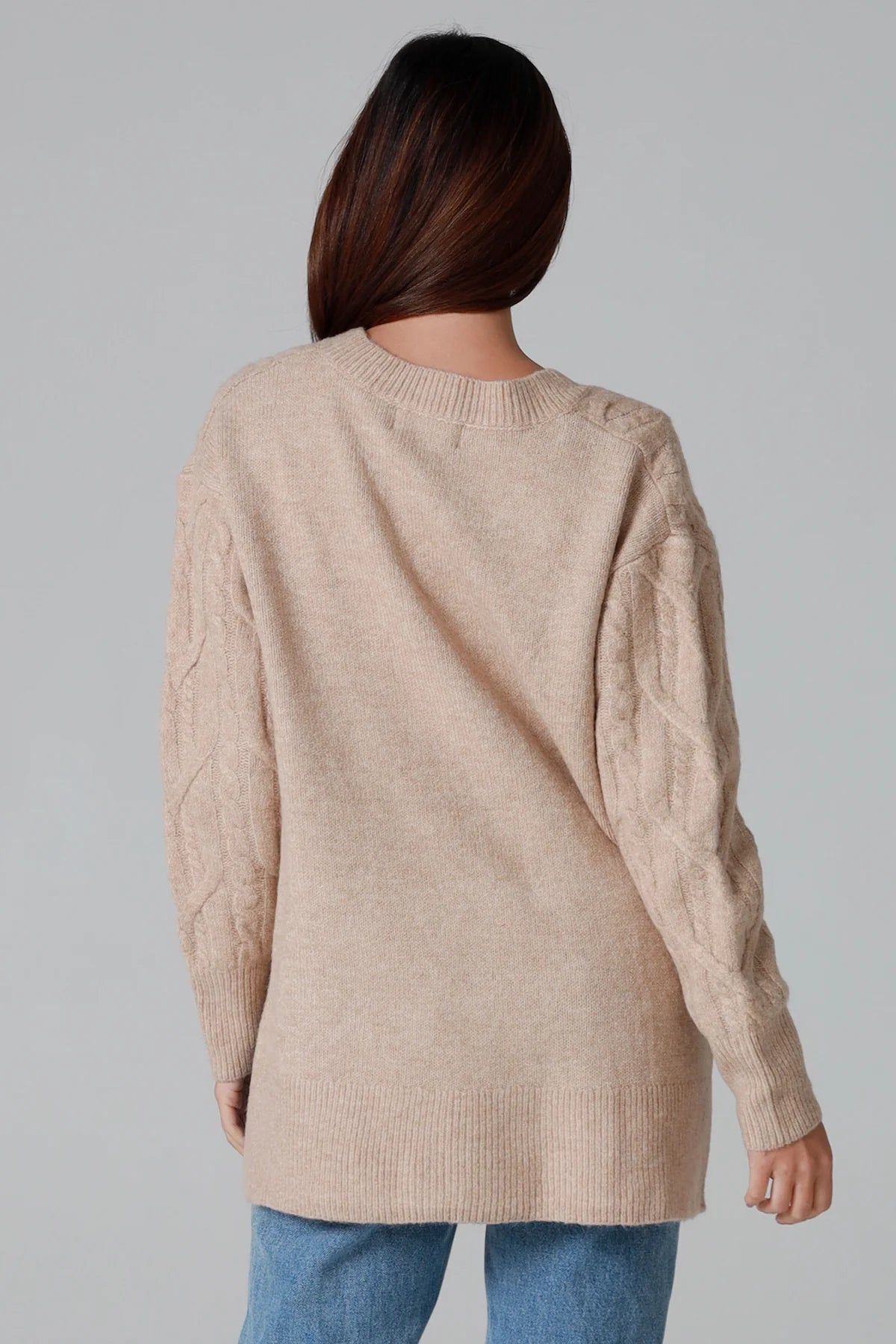 Woman wearing a biscotti colour wool blend cable knit jumper with relaxed fit and v-neckline - Caldra Knit Jumper Australia.