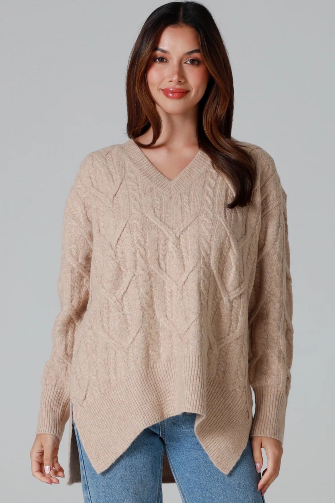 Woman wearing a biscotti colour wool blend cable knit jumper with relaxed fit and v-neckline - Caldra Knit Jumper Australia.