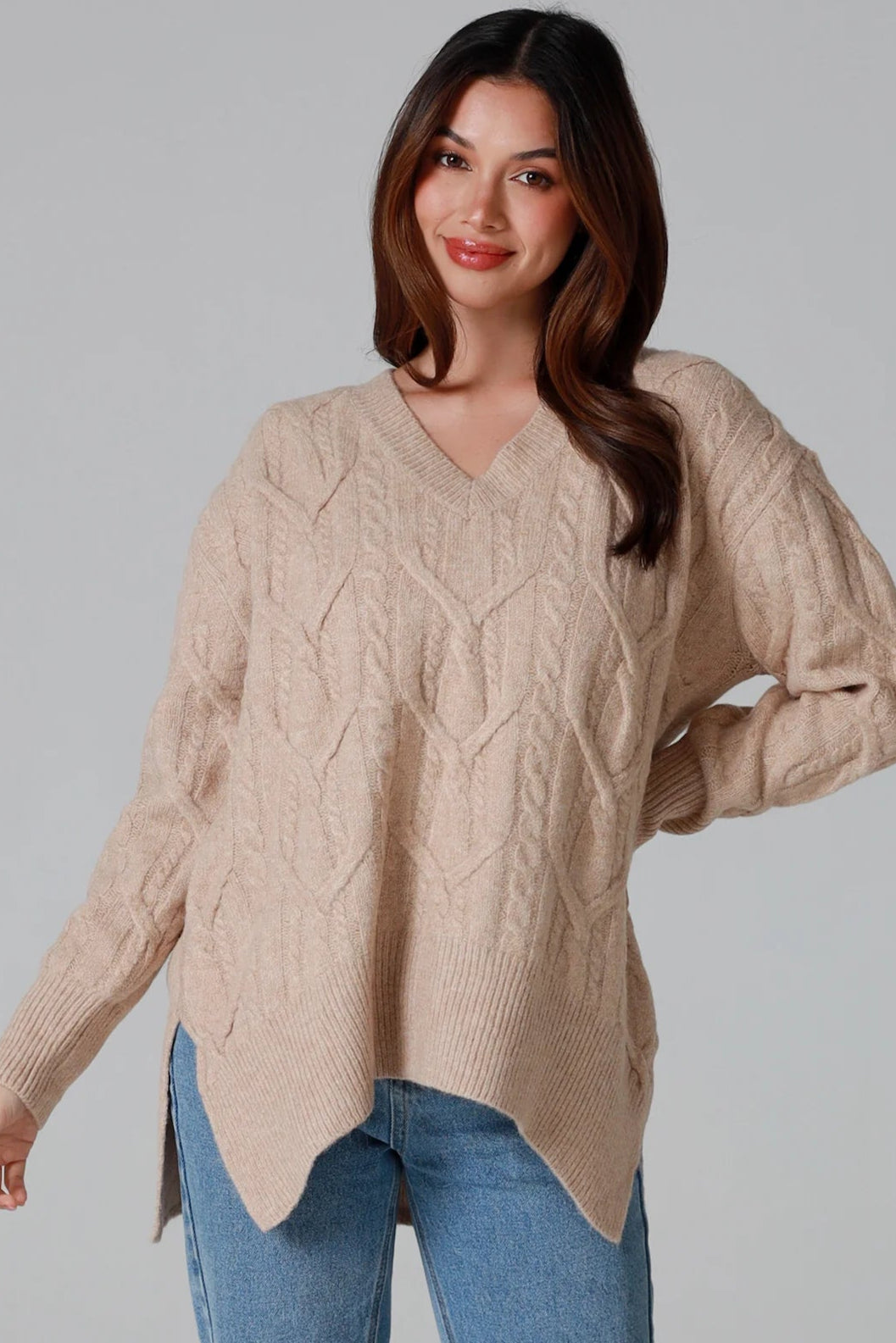 Woman wearing a biscotti colour wool blend cable knit jumper with relaxed fit and v-neckline - Caldra Knit Jumper Australia.