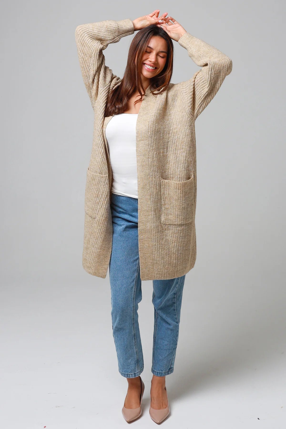 Woman wearing a beige longline knit cardigan with front pockets and jeans - neutral boho knitwear Australia.