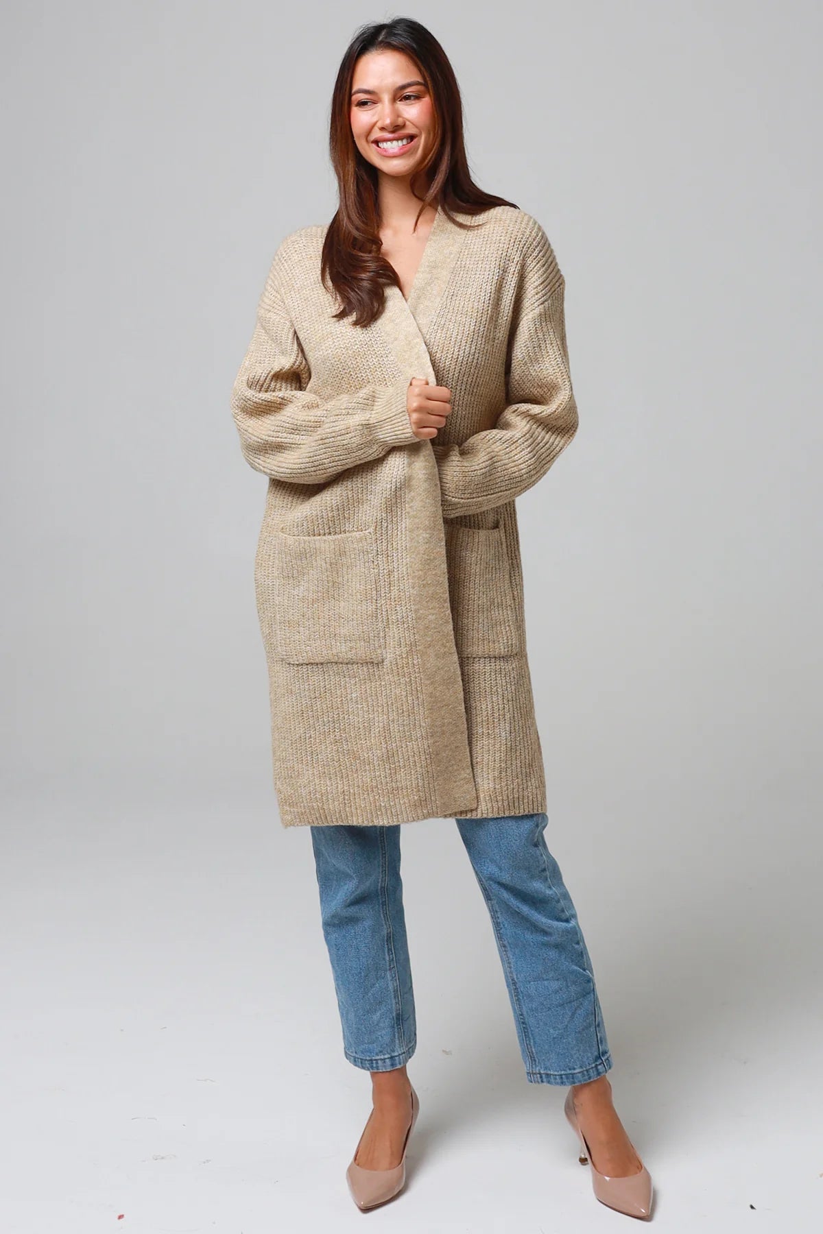 Woman wearing a beige longline knit cardigan with front pockets and jeans - neutral boho knitwear Australia.
