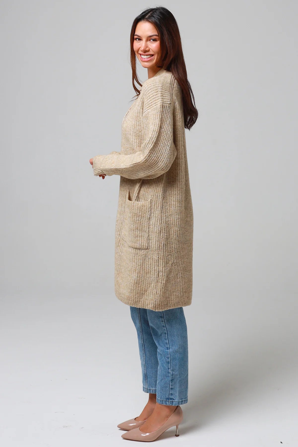 Woman wearing a beige longline knit cardigan with front pockets and jeans - neutral boho knitwear Australia.