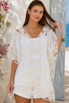 Cream crochet boho kaftan with ornate lace panels and relaxed sleeves in a sunlit Mediterranean coastal setting.