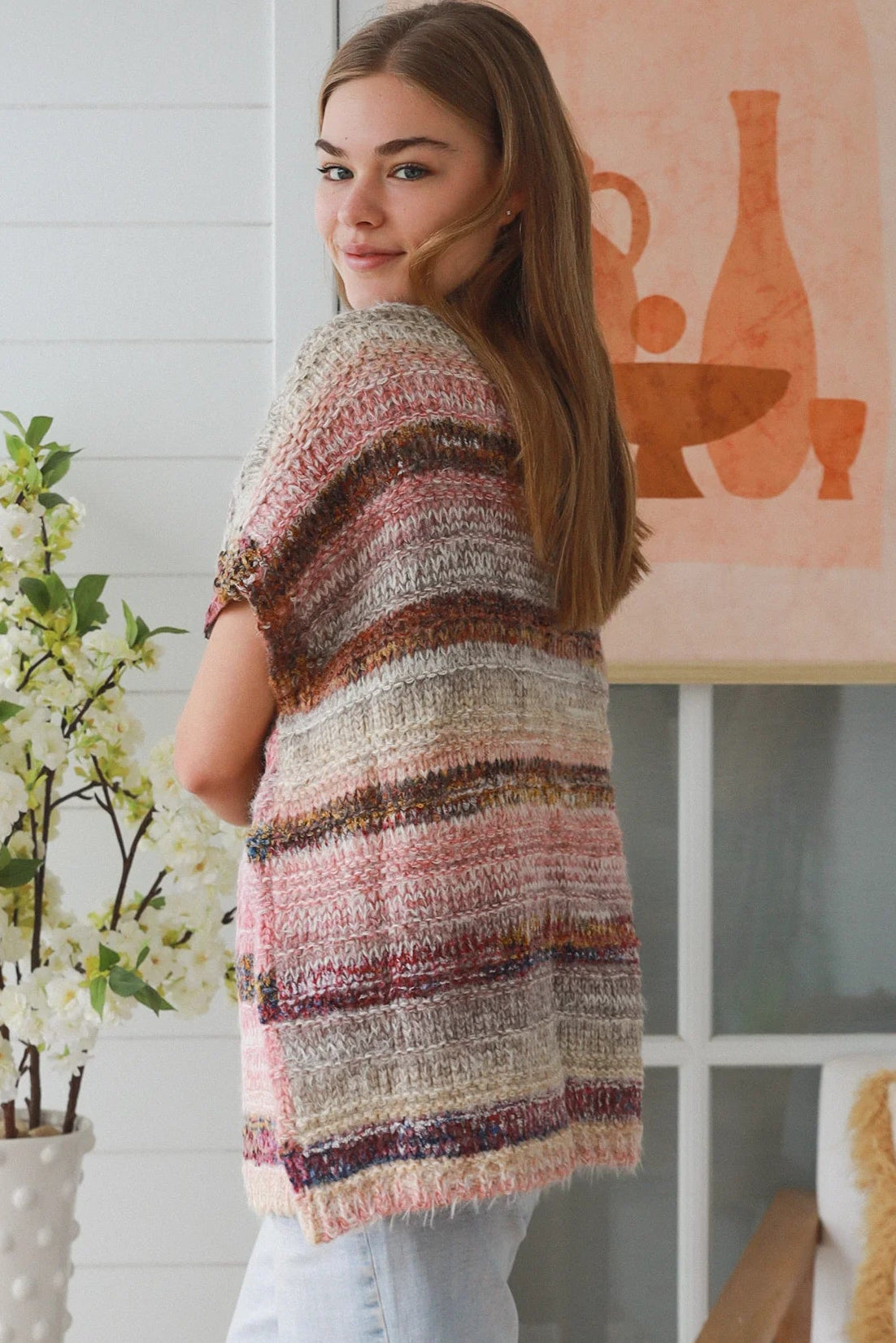 Woman wearing blush marled knit vest with textured finish layered over white top in natural indoor light