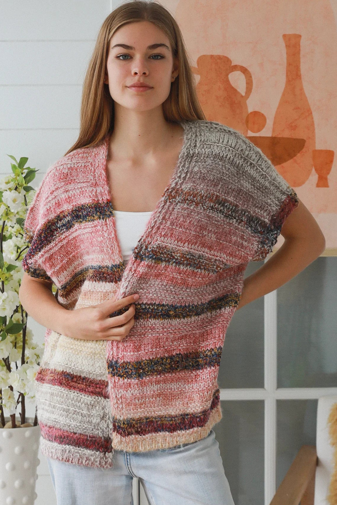 Woman wearing blush marled knit vest with textured finish layered over white top in natural indoor light