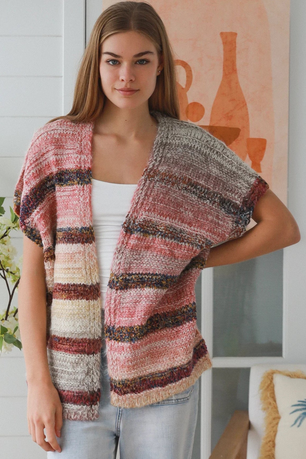 Woman wearing blush marled knit vest with textured finish layered over white top in natural indoor light