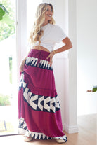 Woman wearing a white top and a long, patterned skirt with geometric designs indoors.