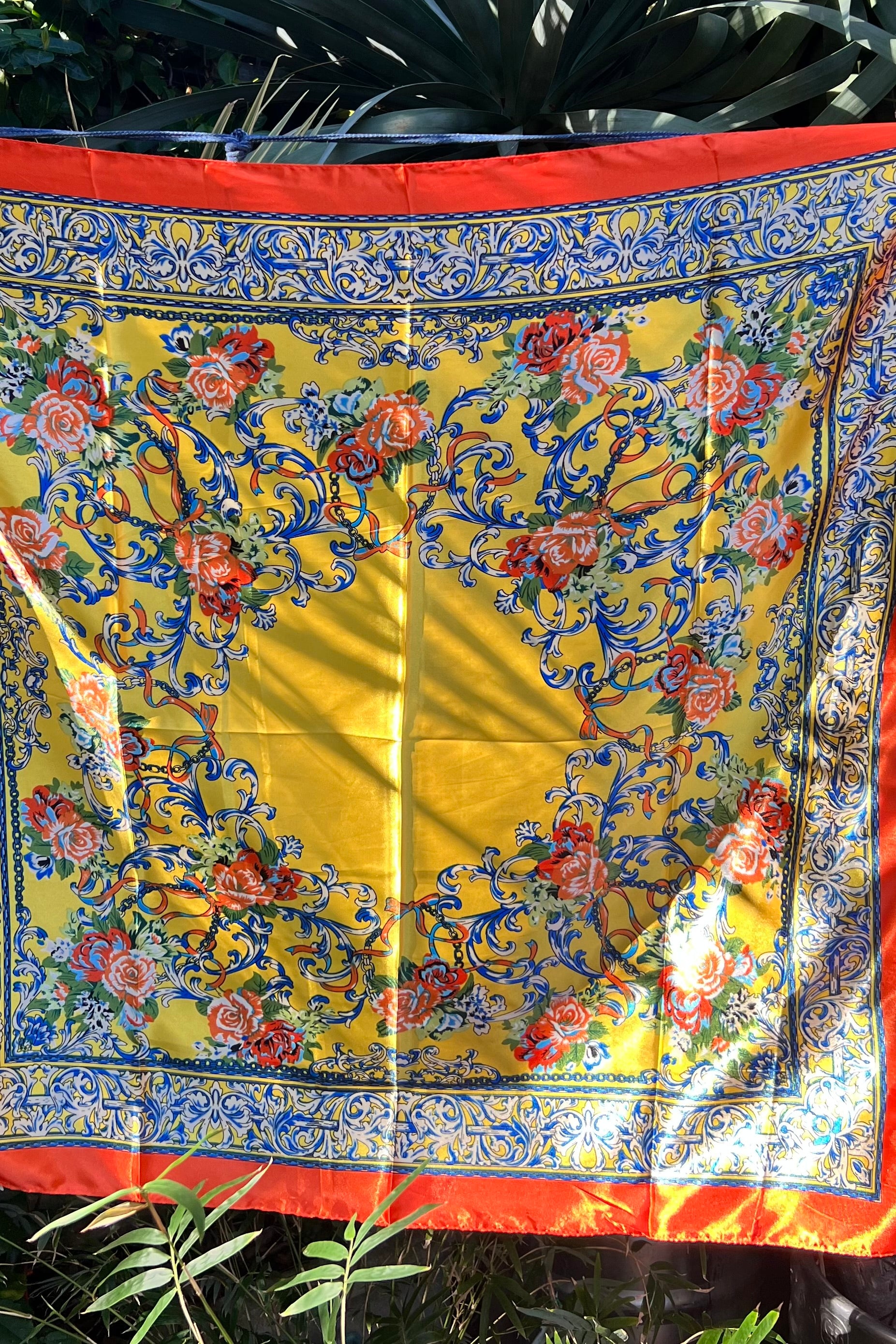 Yellow satin scarf with blue baroque scrolls and red floral print draped in sunlight - boho satin scarves Australia.
