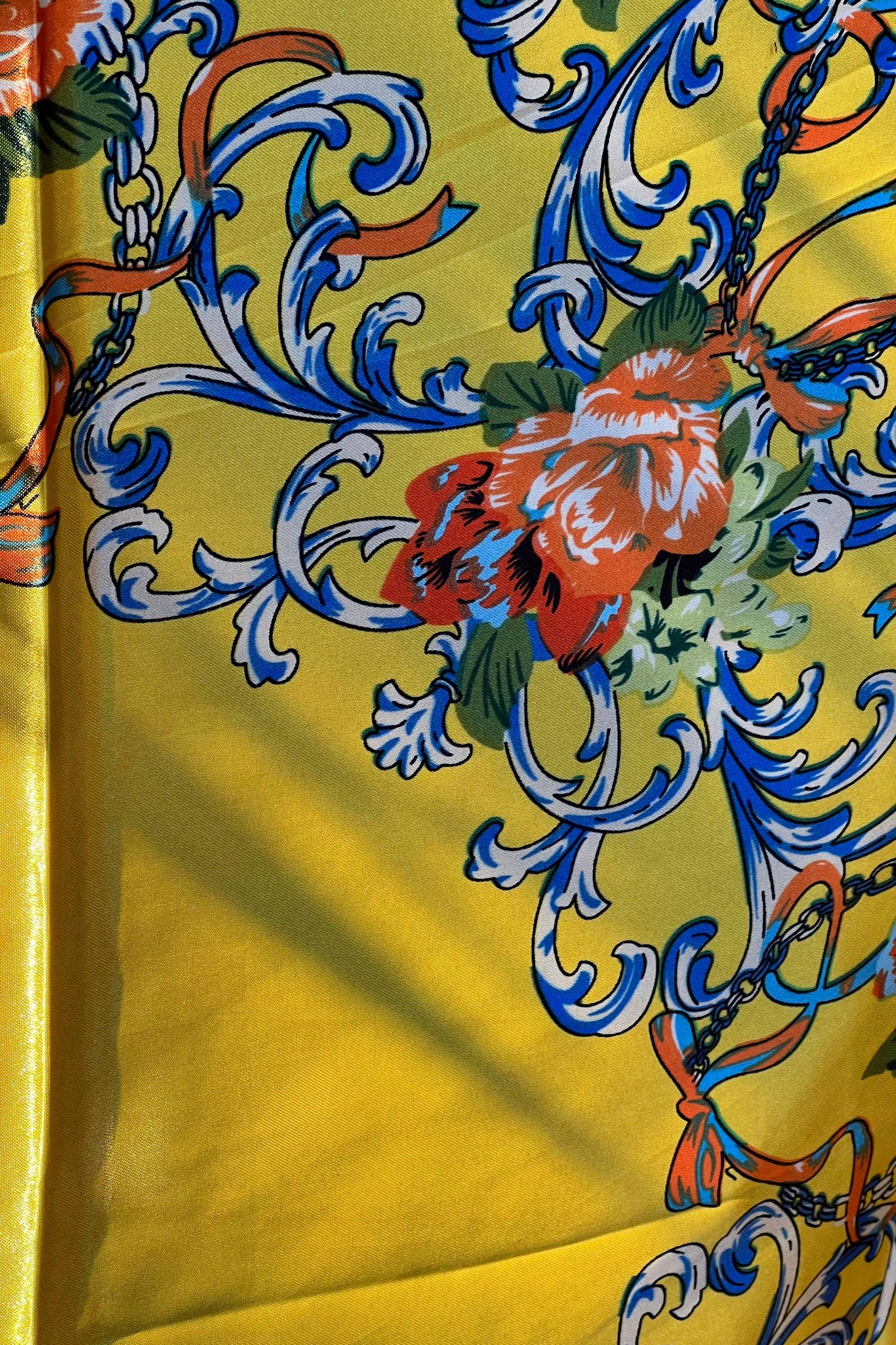 Yellow satin scarf with blue baroque scrolls and red floral print draped in sunlight - boho satin scarves Australia.