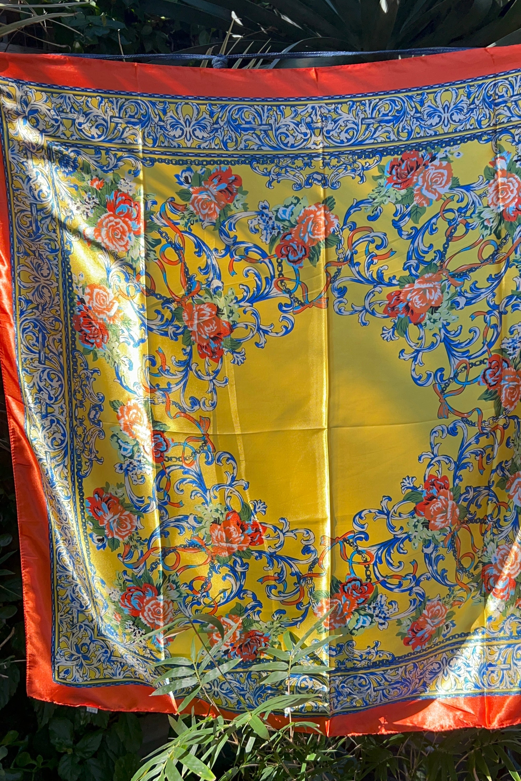 Yellow satin scarf with blue baroque scrolls and red floral print draped in sunlight - boho satin scarves Australia.