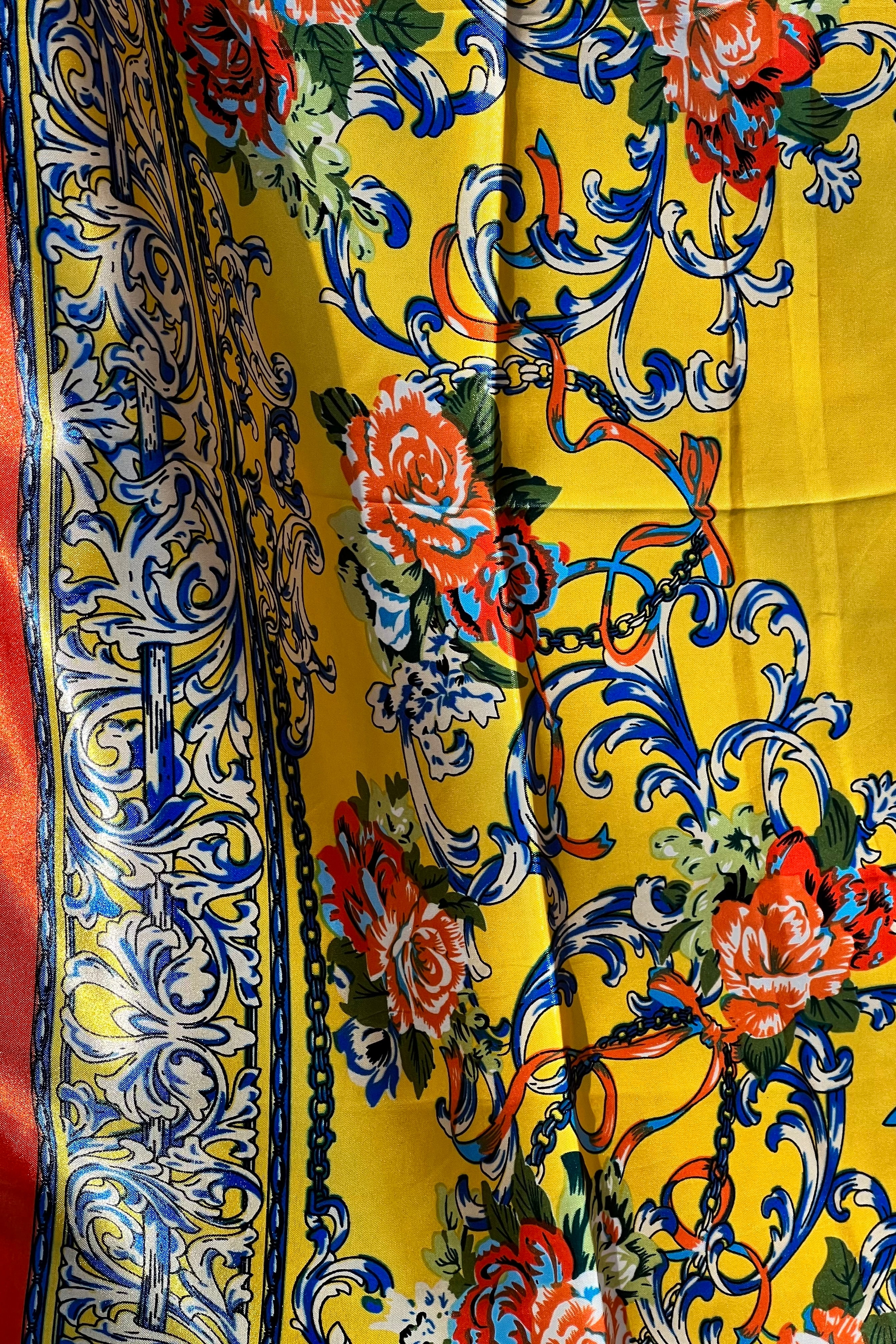 Yellow satin scarf with blue baroque scrolls and red floral print draped in sunlight - boho satin scarves Australia.