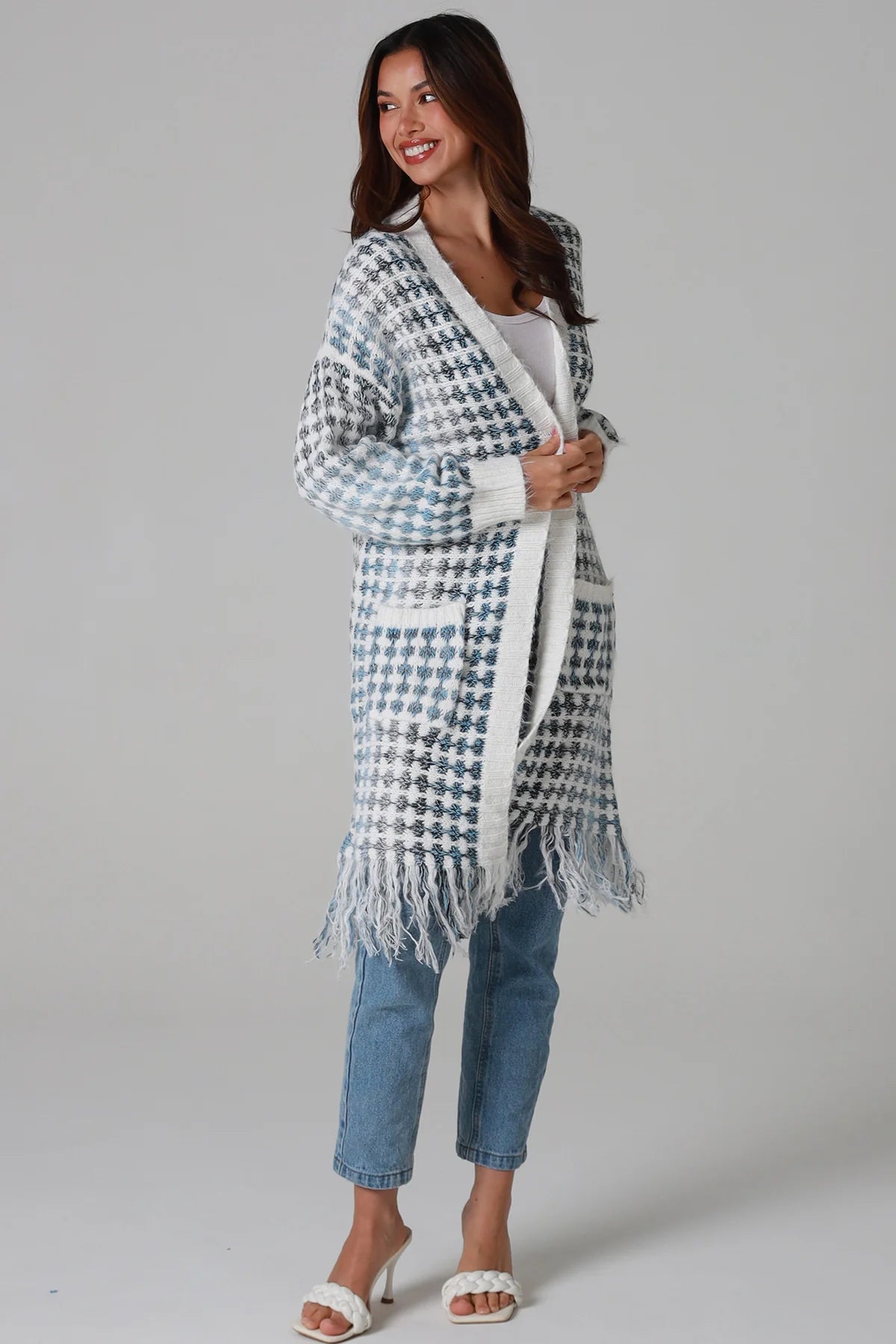 Woman wearing Juliet white and blue houndstooth longline fringe knit cardigan with drop shoulder sleeves, ribbed cuffs and front pockets by Charlotte The Label.