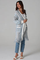 Woman wearing Juliet white and blue houndstooth longline fringe knit cardigan with drop shoulder sleeves, ribbed cuffs and front pockets by Charlotte The Label.